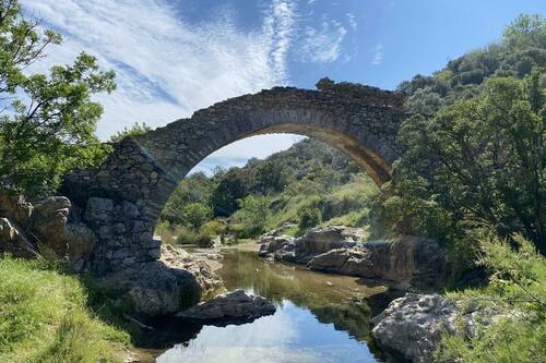 Pont en pierres apparentes enjambant une petite rivière entouré de végétation méditerranéenne