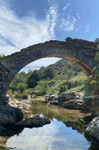 Pont en pierres apparentes enjambant une petite rivière entouré de végétation méditerranéenne
